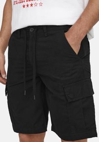 Pantaloni cargo neri realizzati in tessuto misto cotone, dotati di vita con cordoncino, tasche laterali e una tasca con patta sulla gamba.