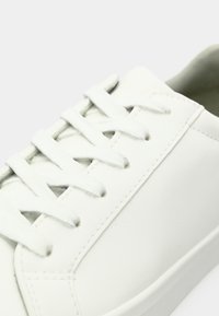 Valge nahast tenniseking valgete paeltega, nähtava õmblusega ja siledal tallal, neutraalsel valgel taustal.