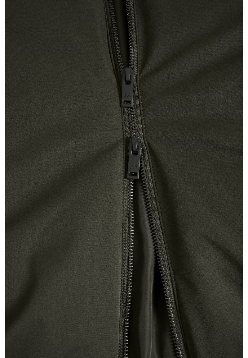 Veste verte à fermeture éclair avec deux zips noirs, texture de tissu lisse et design ajusté avec un léger éclat.