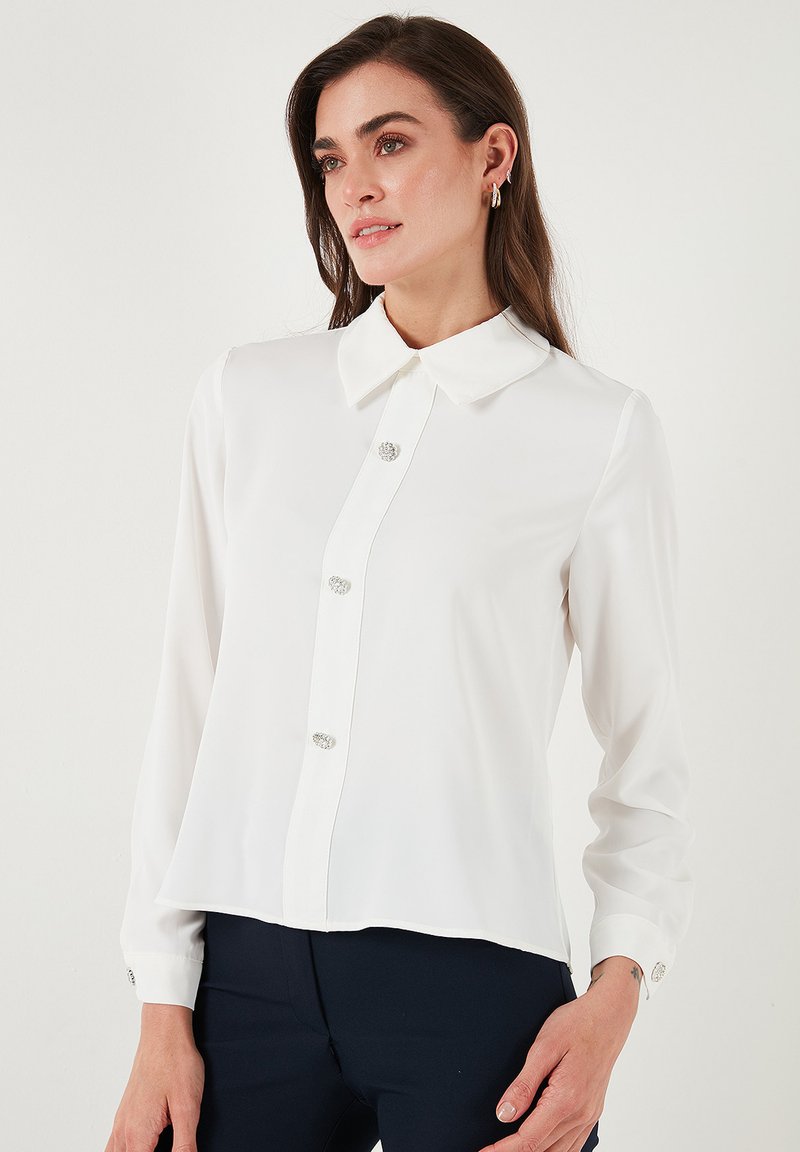 White long-sleeve blouse with a pointed collar, featuring five decorative buttons down the front and buttoned cuffs. Smooth, lightweight fabric.