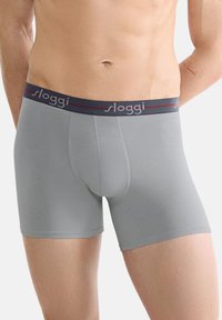 Grå boxershorts med en nära passform, tillverkade av mjukt tyg, med en marinblå midja med "sloggi"-logotyp och subtila röda detaljer.