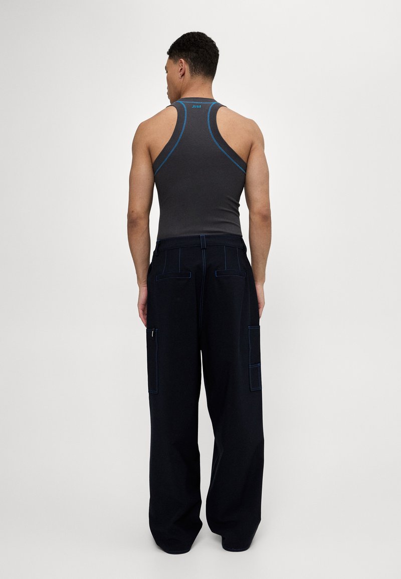 Graues Tanktop mit blauen Akzenten, kombiniert mit lockeren schwarzen Cargo-Hosen mit großen Taschen und kontrastierenden Nähten. Von hinten betrachtet.