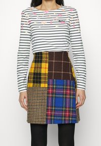 Gestreiftes Langarmshirt mit bunten Tierapplikationen, kombiniert mit einem Patchworkrock, der karierten Mustern in Gelb, Braun, Blau und Plaid zeigt.