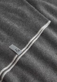 Tessuto di lana grigia con una consistenza morbida, caratterizzato da un bordo a righe bianche e un'etichetta in tessuto grigio con un logo.