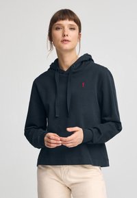 Mörkgrå huvtröja med kenguruficka, dragsko i huvan och röd broderad logga. Mjuk textur och avslappnad passform.