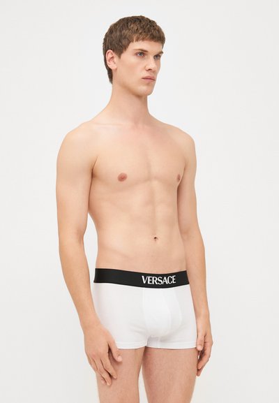 Weiße Boxerbriefs mit einem schwarzen Bund, auf dem der Markenname "VERSACE" in Weiß steht. Aus glattem Stoff mit einer figurnahen Passform.