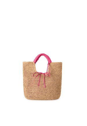 Sac cabas en paille tissée avec des poignées enveloppées de rose et un nœud rose à l'avant, présenté sur fond blanc.