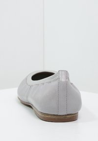 Bailarina de cuero gris con punta redondeada, acentos cosidos y suela plana marrón, que exhibe una textura suave y un diseño minimalista.