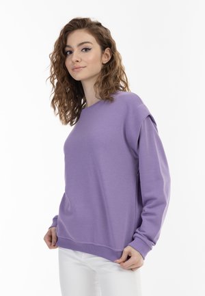 Fioletowy sweatshirt o luźnym kroju, z okrągłym dekoltem i długimi rękawami, wykonany z miękkiego materiału. Posiada ściągacze przy mankietach i u dołu dla dodatkowego komfortu.