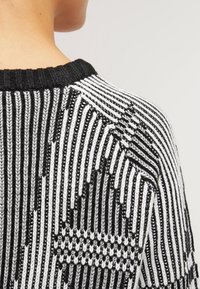 Svart och vit stickad tröja med ett geometriskt mönster av alternerande ränder och zigzags; ribbat halsband och texturerad tyg.