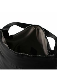 Zwarte handtas met ritssluiting en een zachte buitenkant, voorzien van een gladde stoftextuur en een ruime beige binnenkant. Stevige zwarte handvatten.