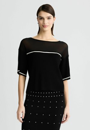 Top negro con un escote barco transparente, mangas cortas con borde blanco. Combinado con una falda negra decorada con tachuelas plateadas.