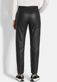Schwarze Lederhosen im Slim-Fit-Stil, mit glatter Textur und taillierter Beinführung. Kombiniert mit schwarzen und metallischen Sneakers.