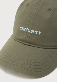Καπέλο σε ελιά πράσινο, κατασκευασμένο από υφασμάτινο υλικό με υφή, με κεντημένο μπλε σήμα "carhartt" στο μπροστινό μέρος, με ραφές και καμπυλωτό γείσο.