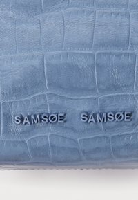 Modrá ražená kožená peněženka s krokodýlím vzorem, s nápisem "SAMSEØ SAMSØE" v tmavší modré barvě. Hladký povrch, minimalistický design.