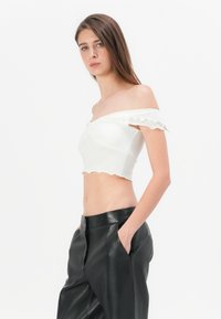 Hvit off-the-shoulder crop topp med bølget kant; glatt tekstur. Kombinert med høyt liv svarte skinnbukser med sidelommer.