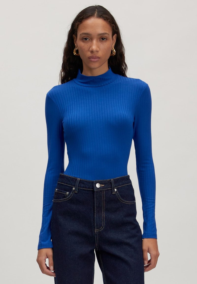 Langärmliges, geripptes Oberteil in lebhaftem Blau, mit hohem Kragen und figurbetontem Design, kombiniert mit dunkelblauen, hoch taillierten Jeans.