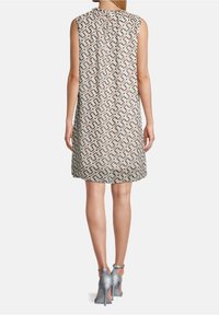 Bezramenné vzorované šaty v krémové, hnědé a šedé geometrickém designu; texturovaná tkanina s plisováním na výstřihu; doplněné šedými sandály na vysokém podpatku.