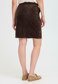 Jupe en velours côtelé marron avec des côtes verticales, coupe droite, mi-longue, et taille élastique ; accompagnée de chaussures beiges à enfiler.