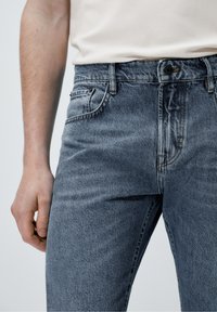 Denimjeans i blekblått med en klassisk design med fem fickor, med en knappstängning och lätta texturdetaljer på tyget.