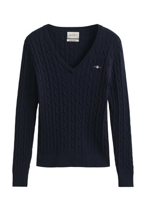 Tmavomodrý sveter so vzorom z pletených vrkôčikov, véčkovým výstrihom a dlhými rukávmi. Má rebrované manžety a lem, s malým vyšívaným logom na hrudi.