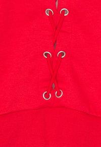 Sudadera con capucha roja con cordones cruzados en la parte delantera asegurados con ojales plateados; ribetes acanalados. Tejido suave, sin patrones ni adornos adicionales.