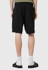 Black cotton shorts with an elastic waistband, knee-length, featuring a smooth texture and a simple design, worn with white socks and sandals.