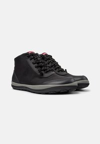Zapatillas altas negras hechas de tela texturizada, con una suela de goma gris, cordones en contraste y una etiqueta con el logo en la lengüeta.