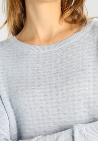Suéter de punto azul claro con un patrón texturizado, cuello redondo y mangas largas. Presenta una tela suave y transpirable.