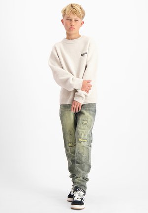 Lichtbeige gebreide trui met ribgebreide mouwen en ronde hals, gecombineerd met versleten groene denim jeans en zwarte sneakers met witte zolen.
