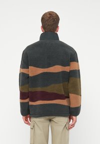 Fleecejacke mit hohem Kragen, mit gewellten Streifen in Dunkelgrau, Ocker, Olivgrün und Burgunderrot. Strukturierten Stoff für Wärme.