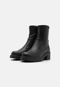 Botas de tobillo de cuero negro con paneles elásticos en los laterales, punta redonda y un tacón grueso. Textura suave con detalles de costura en contraste.
