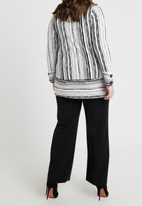 Zwart-wit gestreept shirt met lange mouwen, een hoog-laag zoom en twee knopen bij de manchetten, gecombineerd met zwarte wijde broeken.