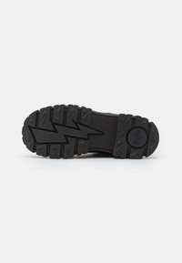 Black rubber sole with deep tread, featuring an angular lightning bolt pattern and circular logo detail on the heel.