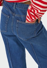 Traperice tamnoplave boje ravnog kroja, s velikim stražnjim džepovima i kontrastnim šavovima duž šavova.