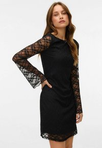 Crna čipkasta haljina s dugim, širokim rukavima. Ima uski kroj i okrugli izrez. Tkanina ima cvjetni uzorak i glatku teksturu.