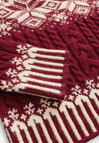 Pull en laine tricotée bordeaux et blanc avec des motifs torsadés et des dessins géométriques sur les manches et le corps.