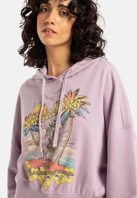 Felpa lilla con stampa grafica che presenta palme, uno scheletro e accenti colorati. Tessuto morbido con vestibilità relaxed e tasca frontale a marsupio.