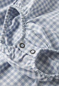 Sinivalkoinen ruudullinen kangas, jossa kootut kuminauhareunat ja kaksi mustaa metallinepparia. Pinta on teksturoitua puuvillaa, jossa on ruudullinen kuvio.