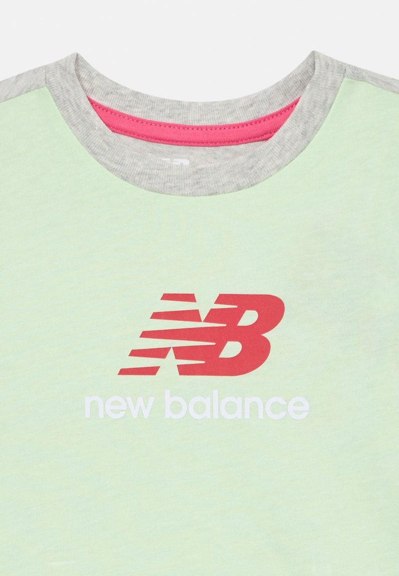Hellgrünes T-Shirt mit einem grauen Rundhalsausschnitt und roten Akzenten, das ein weißes "new balance"-Logo und eine stilisierte rote "NB"-Grafik zeigt.