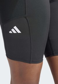 Pantalones cortos deportivos negros de tela elástica, con un diseño ajustado, logo de Adidas en blanco contraste y costuras planas para mayor comodidad.