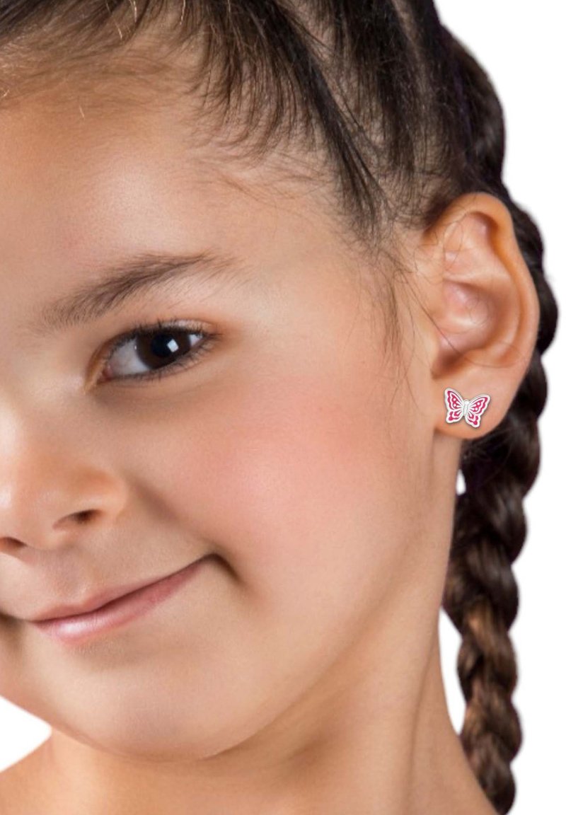 Orecchini a forma di farfalla in rosso e bianco, realizzati in metallo, indossati da una bambina con capelli intrecciati. Design semplice, texture liscia.