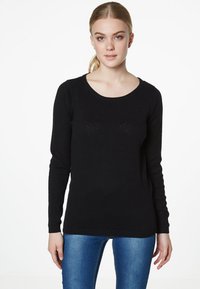 Pull noir à manches longues avec un col rond et un tricot texturé, affichant des motifs horizontaux subtils. Associé à un jean bleu.
