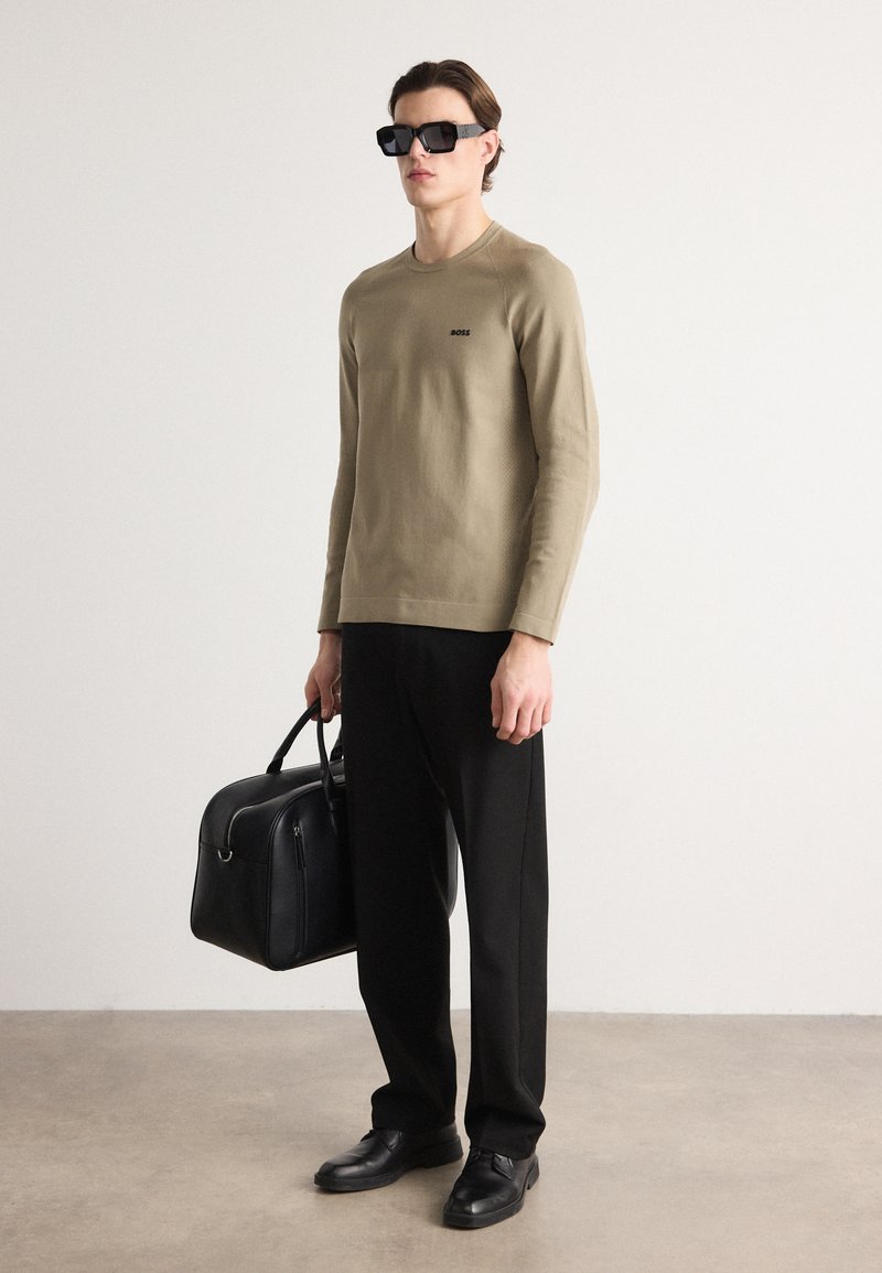 Camisa beige de manga larga con logo, pantalones negros a medida, zapatos de cuero negros y un bolso negro. Unas gafas de sol negras y cuadradas completan el look.