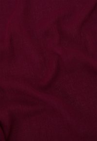 Tessuto bordeaux con una texture liscia, che mostra lievi pieghe e variazioni di colore. Materiale leggero e traspirante.