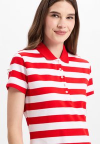 Rood-wit gestreepte polo-shirt met korte mouwen, een platte kraag en vijf knoopsluitingen. De stof heeft een gladde textuur.