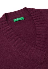 Burgunderfarbener Strickpullover mit geripptem V-Ausschnitt und strukturiertem Stoff. Das Etikett trägt die Aufschrift "United Colors of Benetton" in grün.