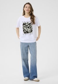 White t-shirt featuring a black and cream graphic design with the text “GRAPHIC EDITION.” Paired with light-wash flared jeans and casual shoes.