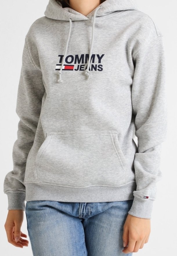Felpa grigia con tasca a marsupio e cappuccio regolabile con coulisse. Presenta il logo "TOMMY JEANS" in blu navy e rosso sul petto. Polsini e orlo a costine.