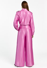 Roze satijnen tweedelige outfit bestaat uit een top met lange mouwen en kraag en een broek met wijde pijpen. Gladde textuur met een subtiele glans.